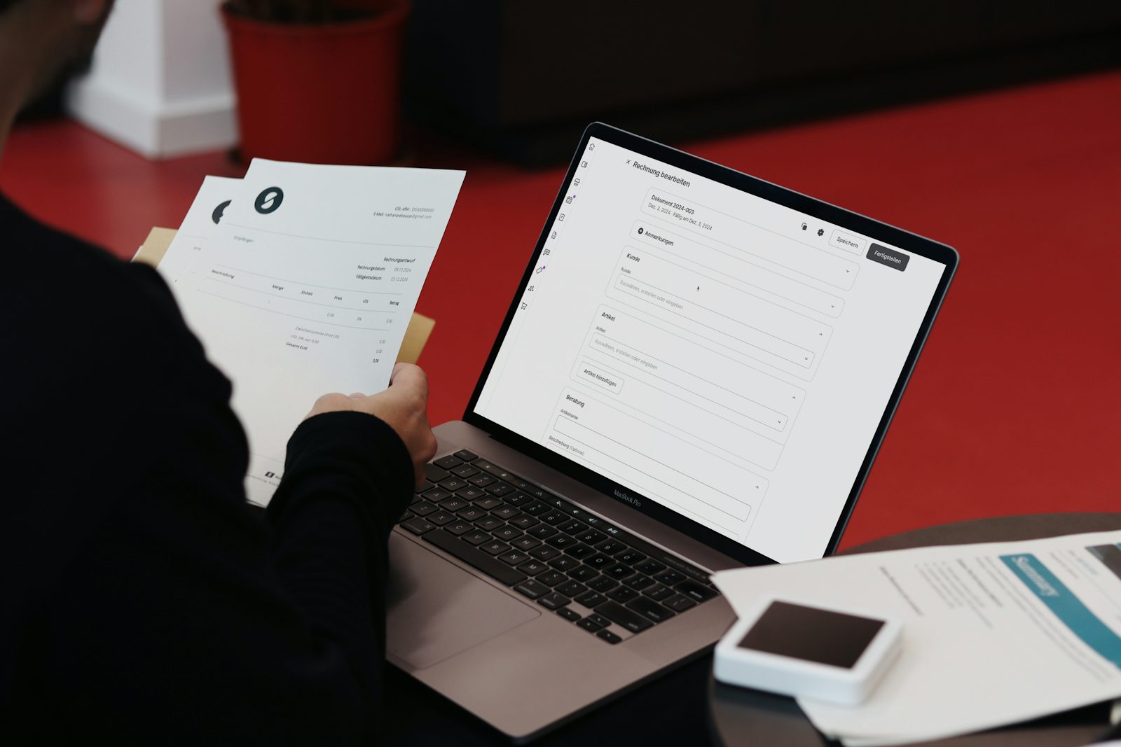 A person at a desk working on a laptop next to printed paper documents