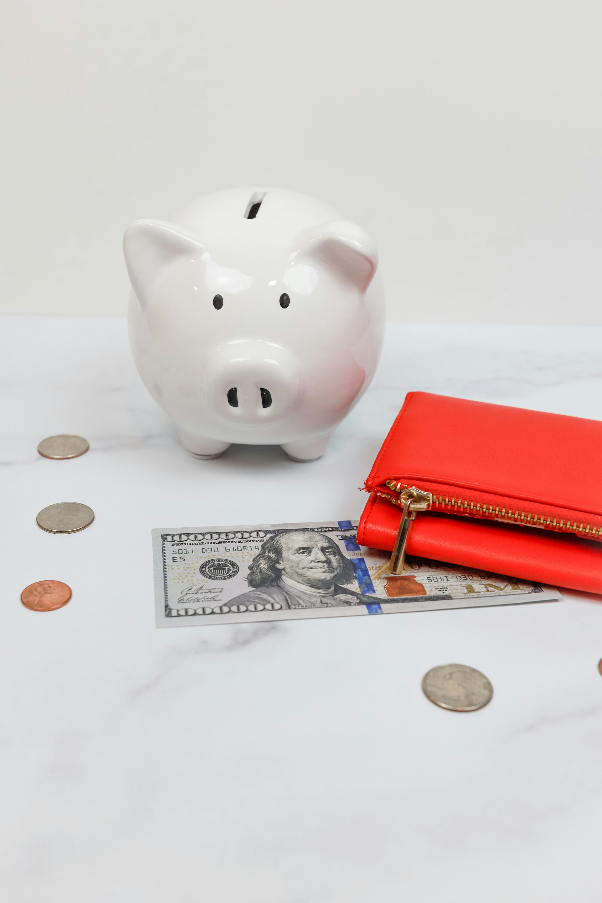 A pink piggy bank surrounded by scattered coins on a desk