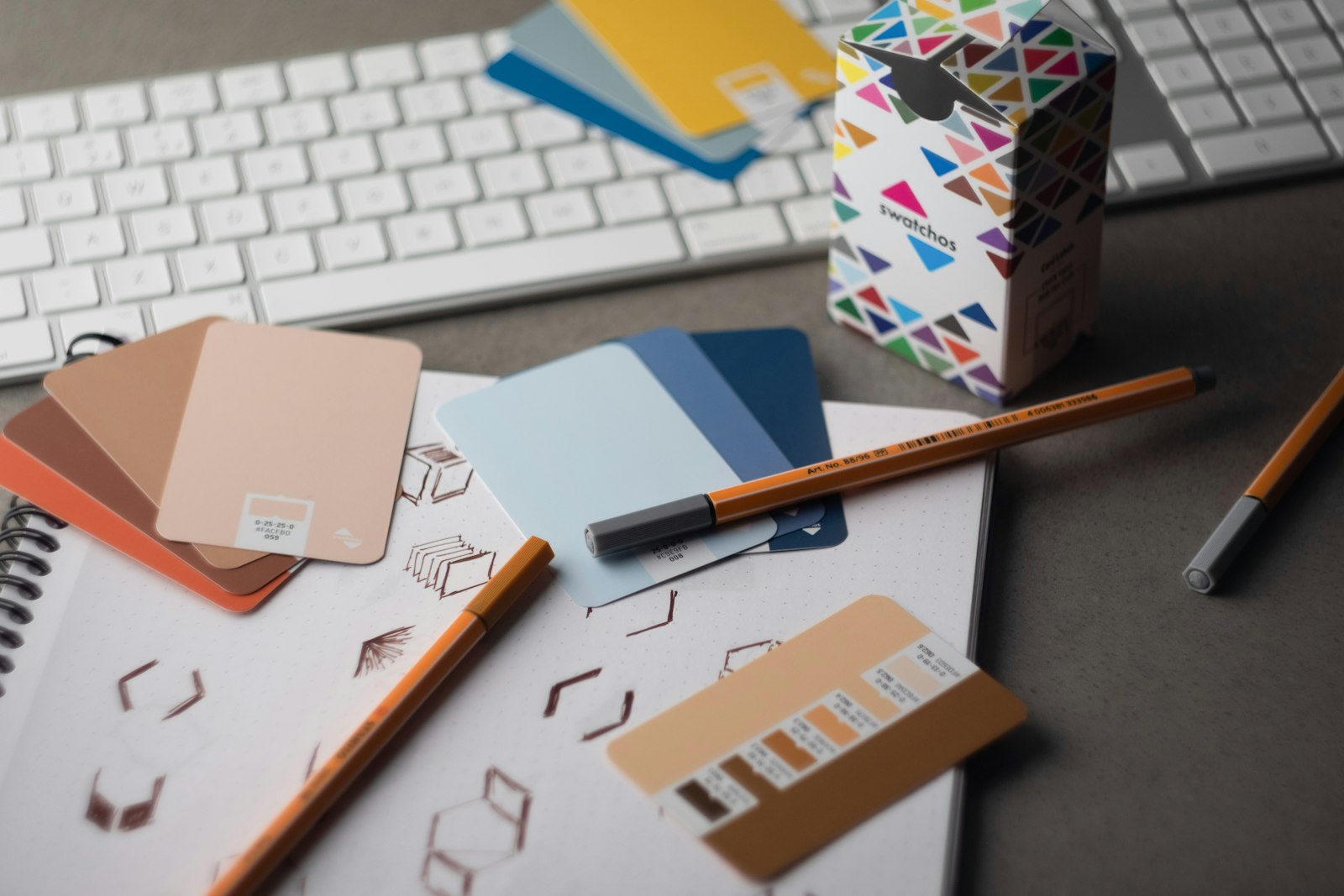 A graphic designer's desk with a keyboard, pencils, and printed colour swatch cards