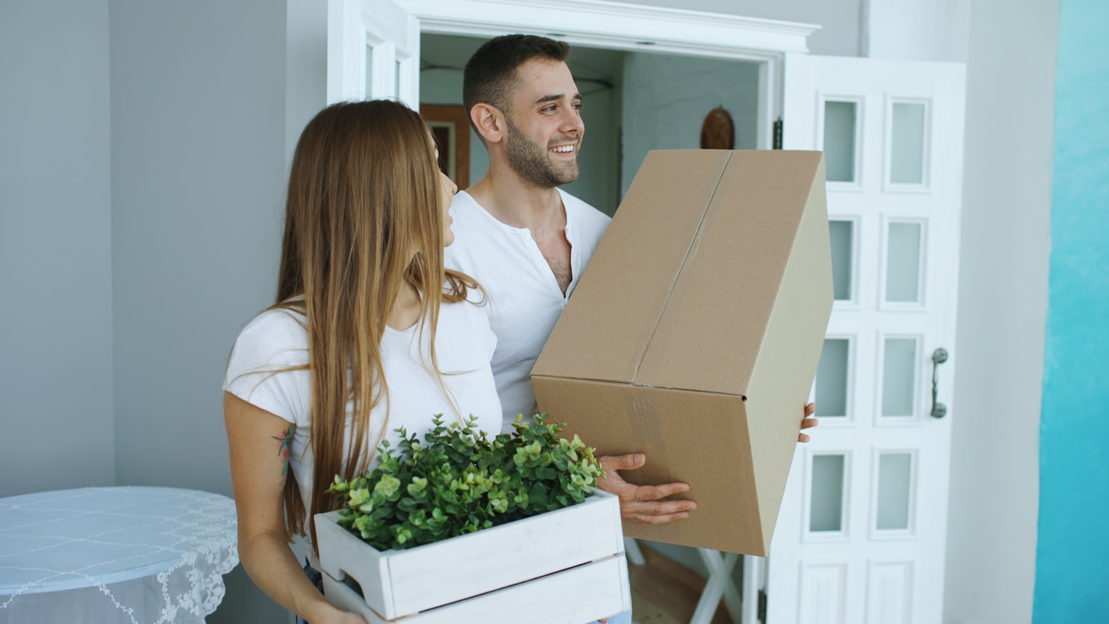 A couple carrying cardboard moving boxes into a new space