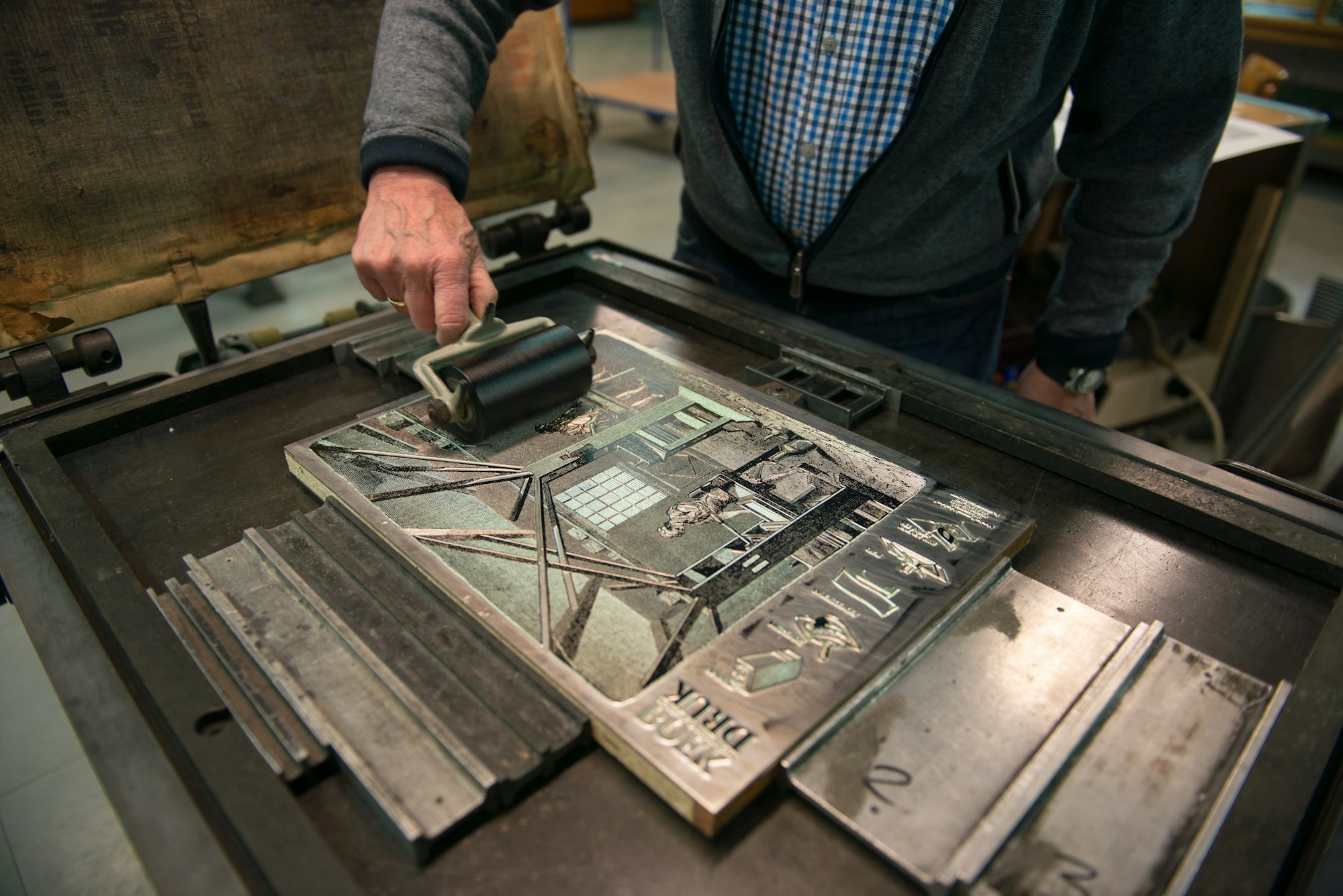 Hands inking a printing form on a vintage letterpress press